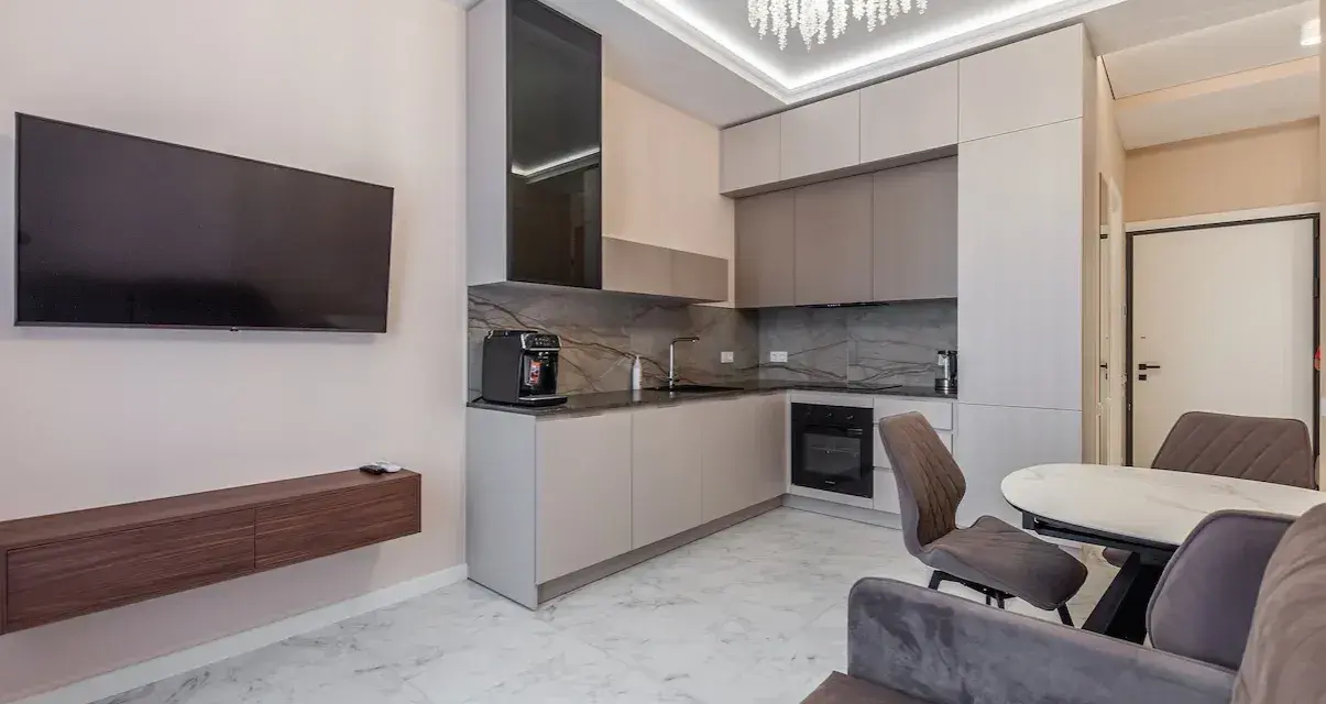 Un moderno open space lungo e stretto con cucina a vista, zona TV e tavolo da pranzo.