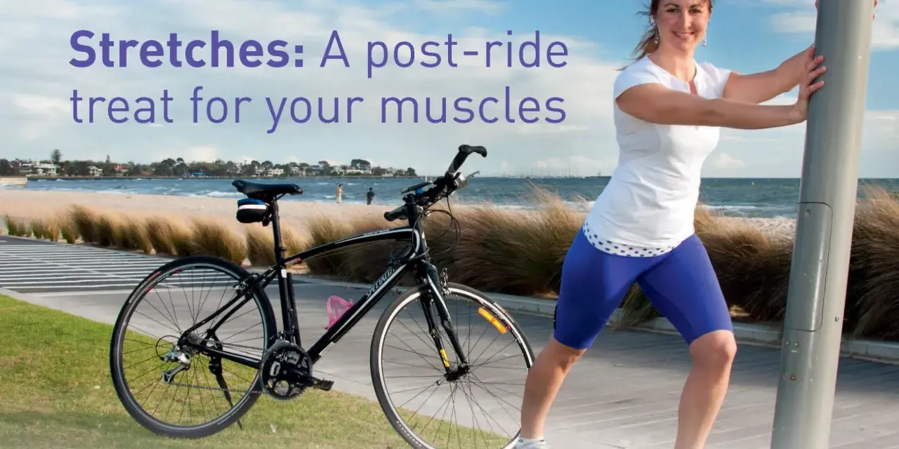 A woman performs a bicycle stretch, leaning on a pole after a ride by the beach.
