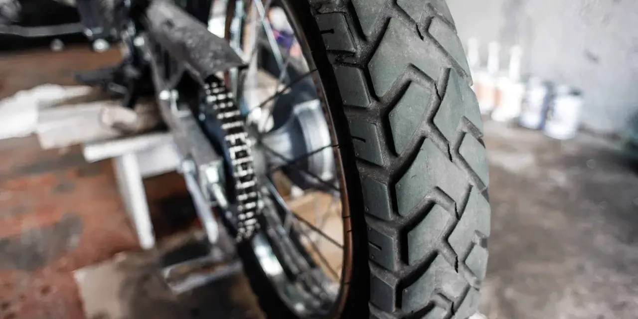 Zbliżenie na bieżnik motocyklowej opony, gotowej do wymiany. W tle widać fragment motocykla i narzędzia.