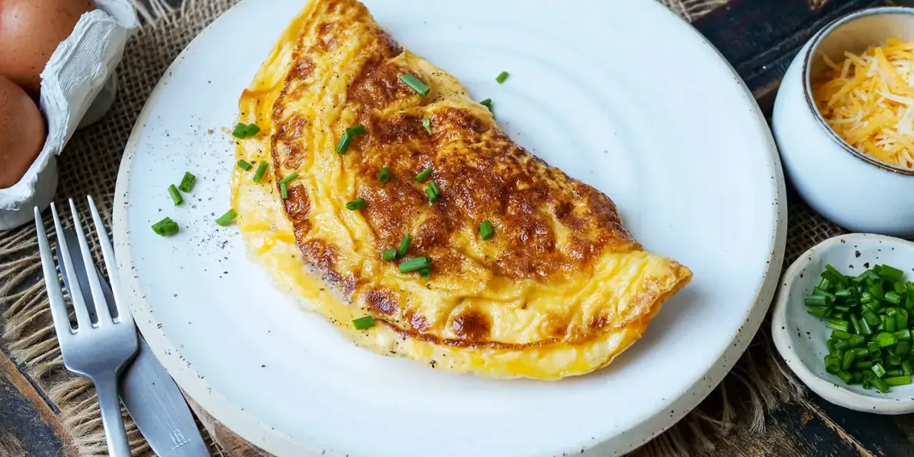 Goldbraunes Omelett mit Käse und Schnittlauch, perfekt für ein schnelles Omelette Rezept. Daneben Eier, Käse und Schnittlauch.