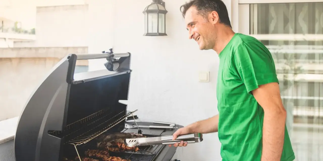 Glad man grillar korv på balkong.