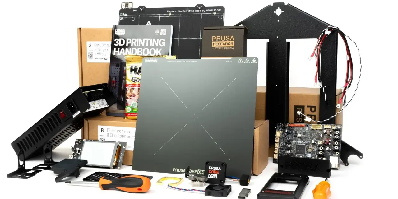 Zestaw części do drukarki 3D Prusa Core One: płyta główna, zasilacz, ekran, instrukcja, elementy konstrukcyjne i akcesoria.