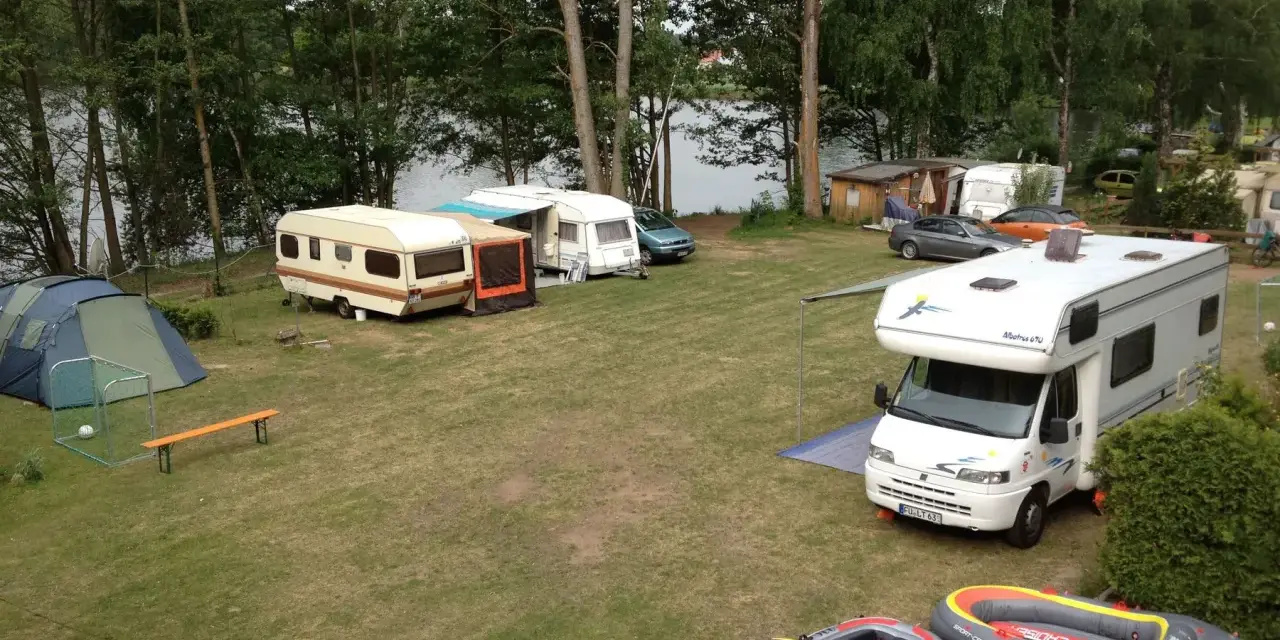 Campingplatz am sonnensee flachslanden mit Wohnmobilen, Wohnwagen, Zelt und Schlauchbooten am Ufer.