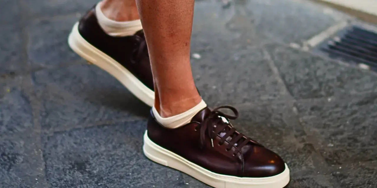 Un uomo indossa sneakers marroni con calze bianche a vista. Un look casual ma curato, perfetto per chi cerca quali calze con sneakers uomo.