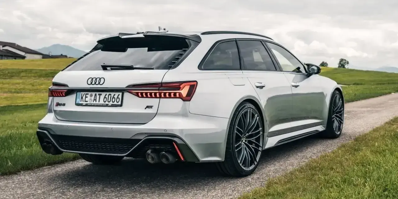 Srebrne Audi RS6 Avant z pakietem ABT na tle zielonych wzgórz. Sprawdź audi rs6 cena i możliwości tego potwora.