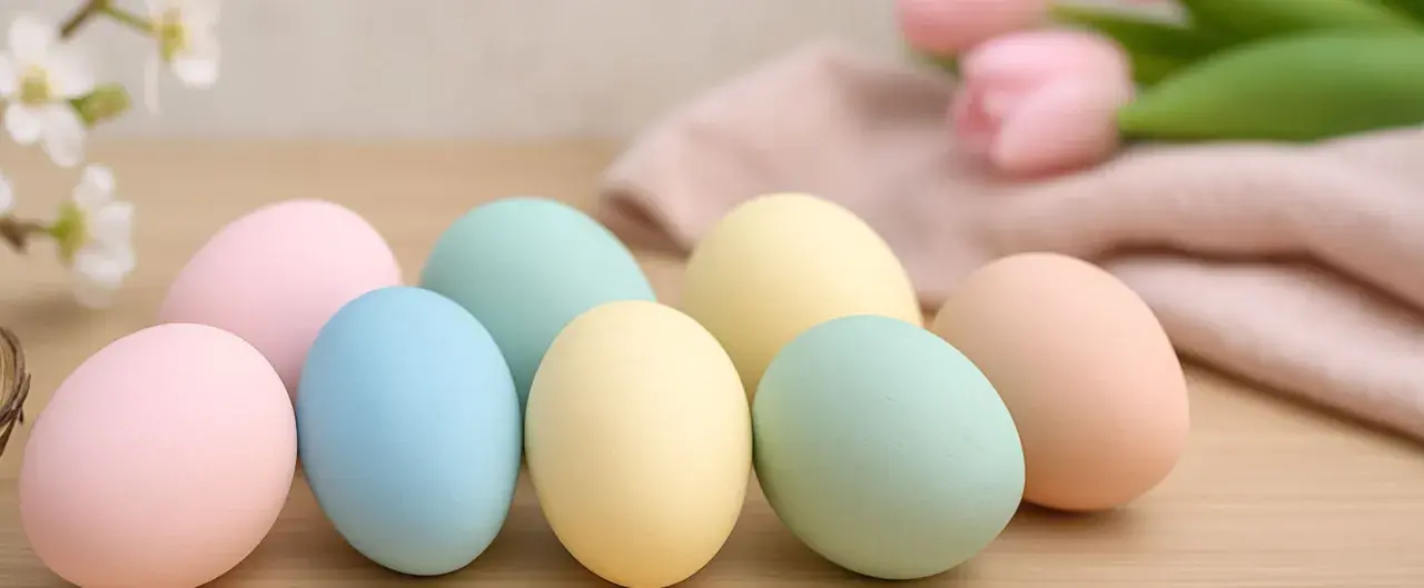 Huevos de pascua para pintar en tonos pastel, listos para decorar. Flores y tela suave al fondo.