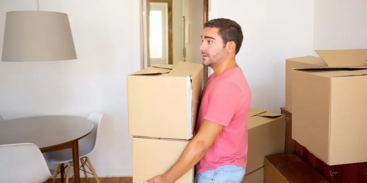 Un homme porte des cartons, prêt à quitter le domicile conjugal. Le propriétaire semble pensif, entouré de cartons de déménagement.