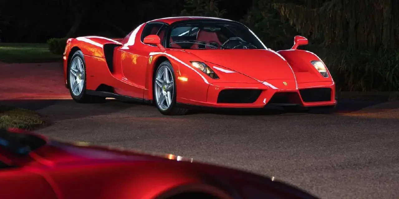 Czerwone Ferrari Enzo zaparkowane nocą na drodze, z innym czerwonym samochodem w tle.