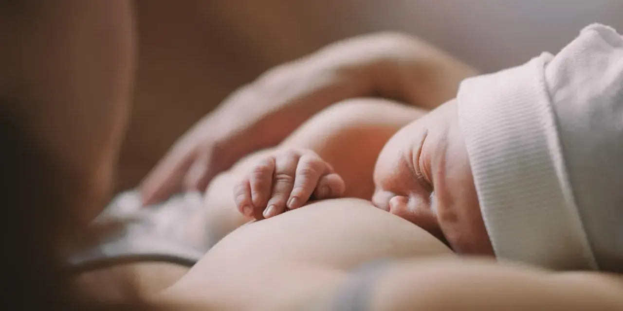 Ein Baby stillt, die kleinen Finger greifen sanft zu. Ein Moment der Ruhe und Verbundenheit.