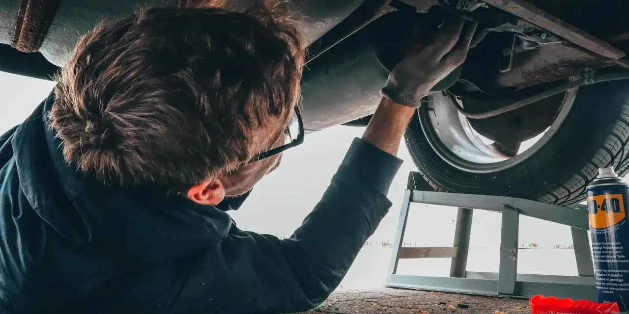Un giovane impara come si diventa meccanico, lavorando sotto un'auto con attrezzi e spray.