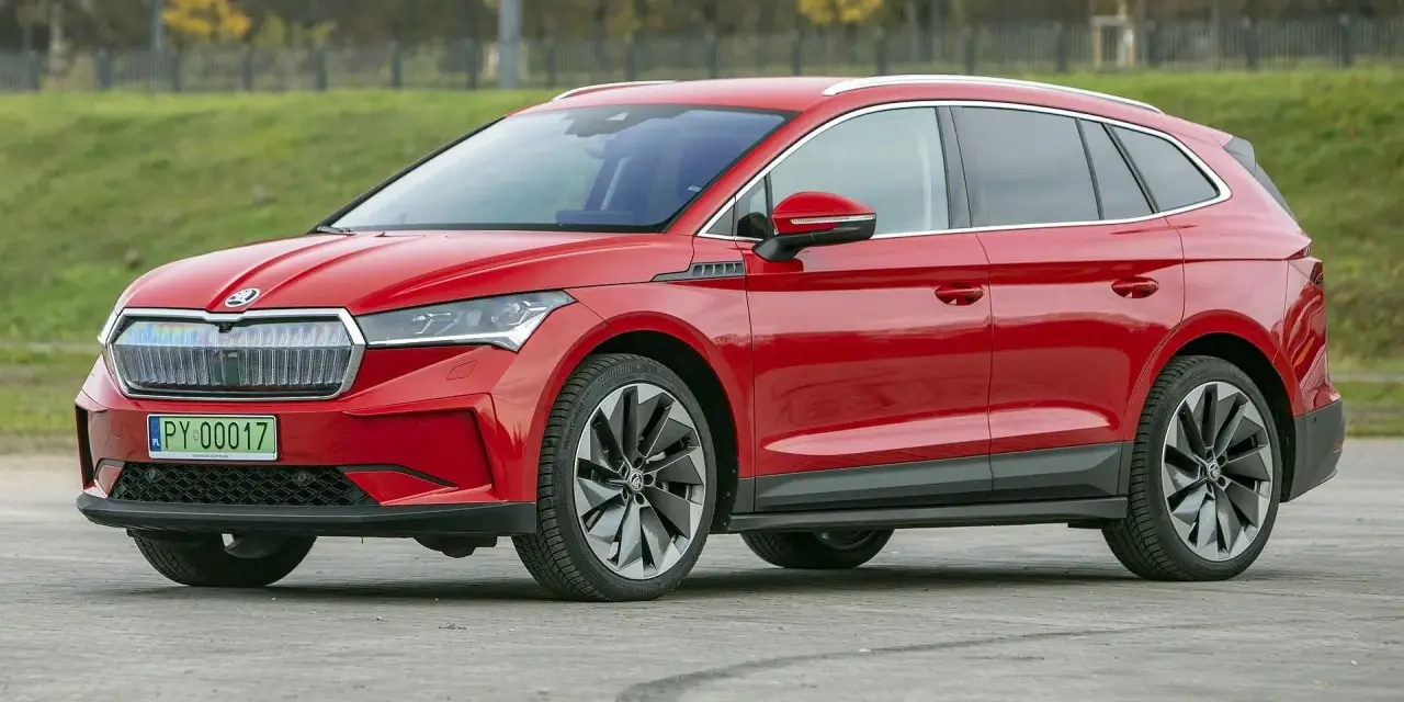Czerwona Skoda Enyaq na tle zieleni, z tablicą rejestracyjną PY 00017. Ten elektryczny SUV oferuje imponujący zasięg.