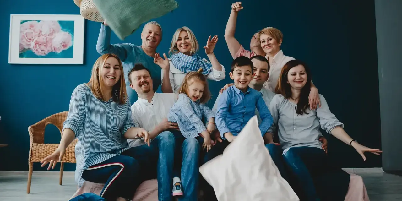 Wesoła rodzina patchworkowa rzuca poduszkami, śmiejąc się i ciesząc wspólnym czasem.