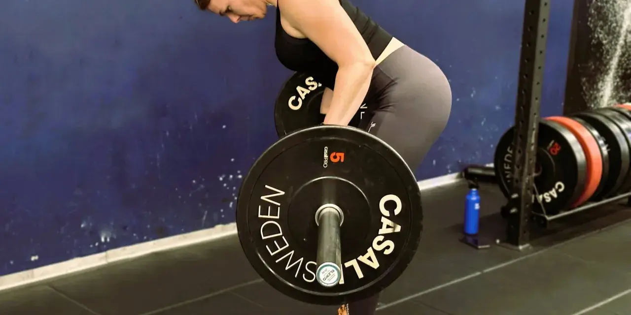 Kvinna utför en t bar row med en skivstång i ett gym.