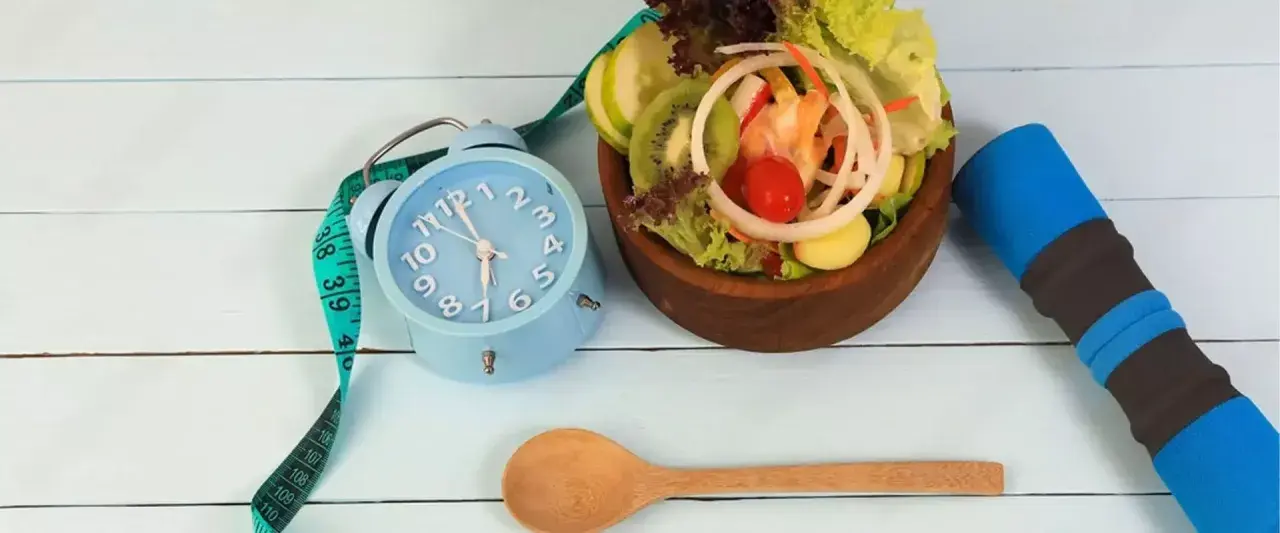 Réveil bleu, ruban à mesurer, salade fraîche et haltère bleu. L'heure est à la forme, jeune 16/8.