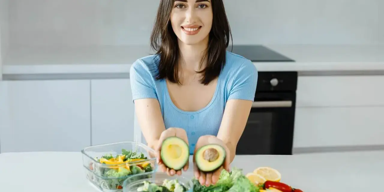 Uśmiechnięta kobieta prezentuje awokado, składnik wielu diet, w tym keto. Jej opinie o keto diecie są pozytywne.