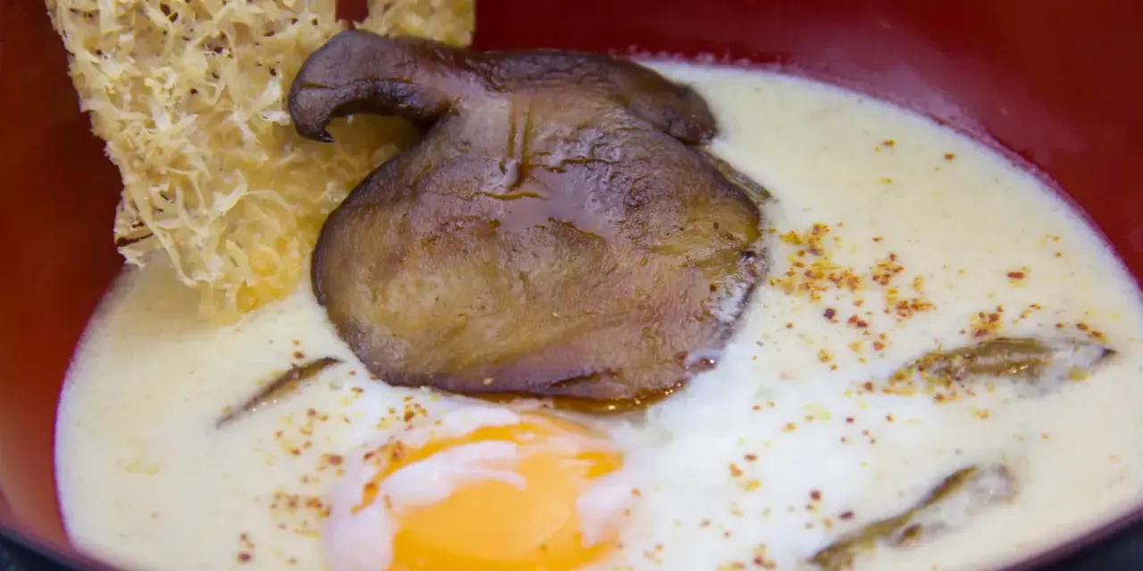 Un œuf parfait, crémeux et onctueux, baigne dans une soupe onctueuse, garnie d'un champignon poêlé et d'une tuile croustillante.