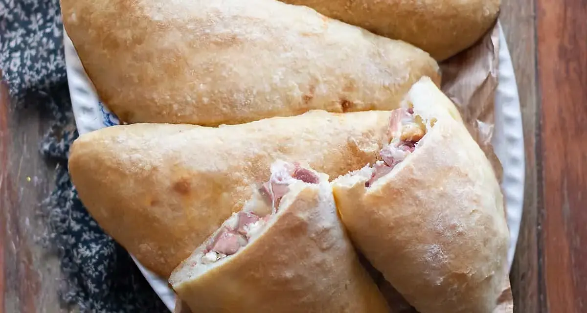 Calzoni al forno dorati e fragranti, ripieni di prosciutto e formaggio filante, pronti per essere gustati.