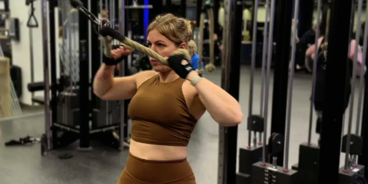 Kvinna utför stående rodd med kabelmaskin. Hon fokuserar på träningen i gymmet.