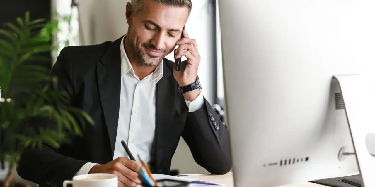 Uomo d'affari al telefono, scrive appunti. Potrebbe essere un agente immobiliare che discute di quanto guadagna un agente immobiliare.