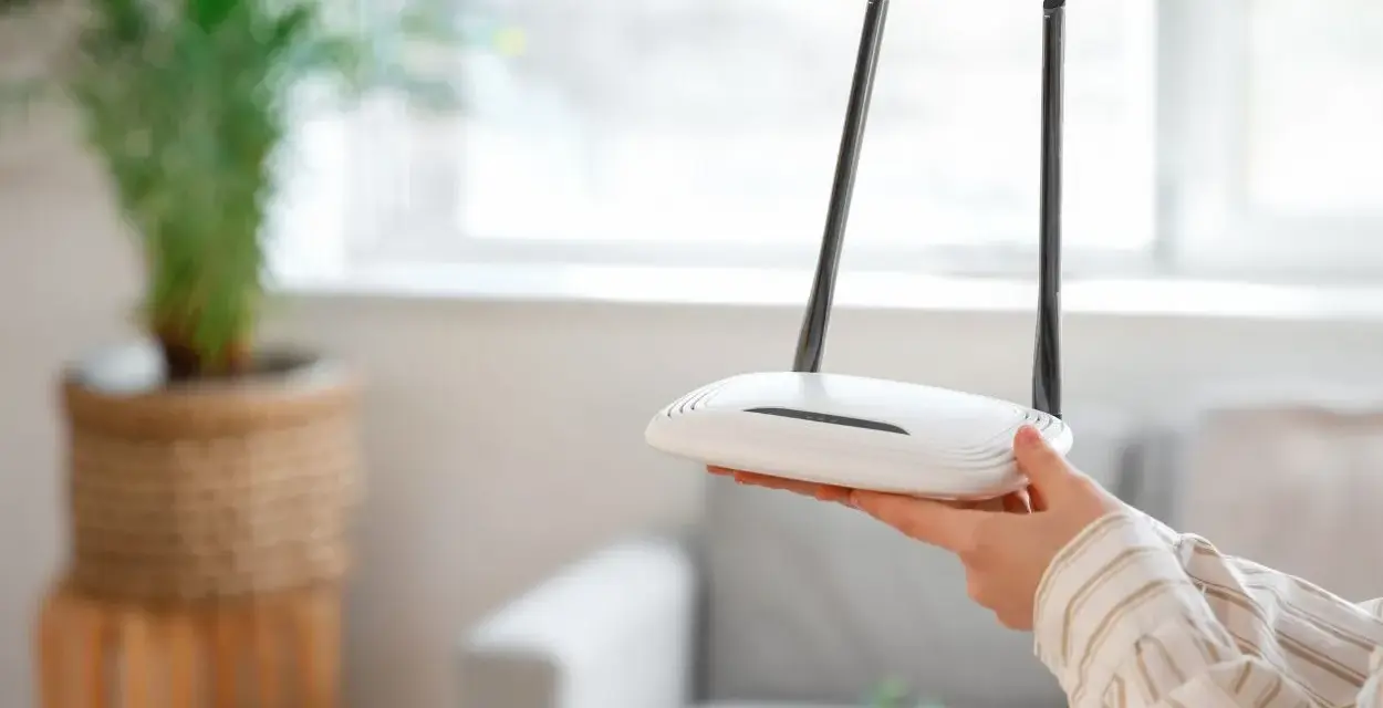 Dłoń trzyma biały router z dwiema antenkami. Dowiedz się, jak zresetować router, aby rozwiązać problemy z siecią.