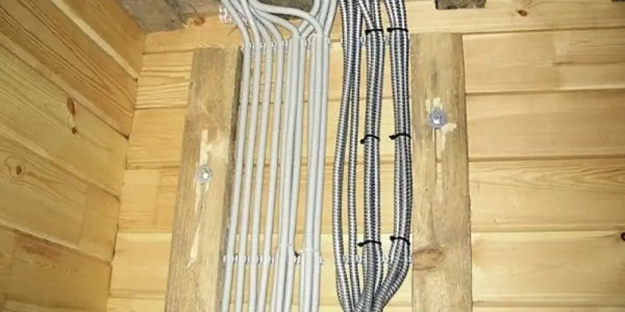 Instalacja elektryczna w domu drewnianym schemat: wiązki kabli w peszlach wychodzące z sufitu, przymocowane do drewnianych belek.