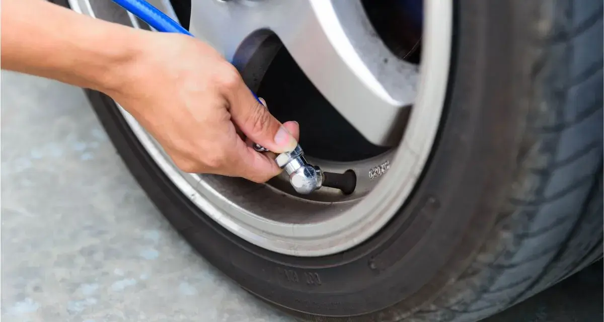 Mano che collega un tubo blu alla valvola di un pneumatico per controllare la pressione gomme auto.
