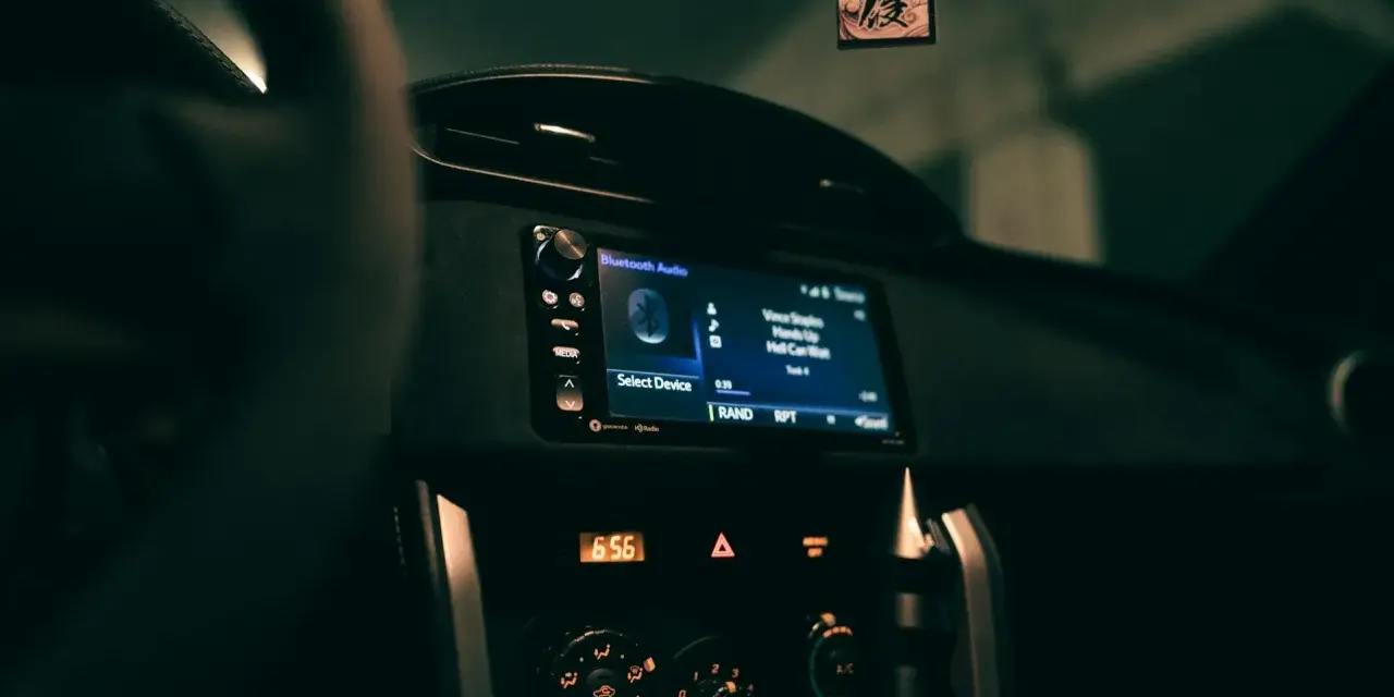 Wnętrze samochodu z włączonym radiem, na ekranie wyświetla się "Bluetooth Audio" i tytuł piosenki. Zastanawiasz się, co to jest treble w kontekście dźwięku? To wysokie tony.
