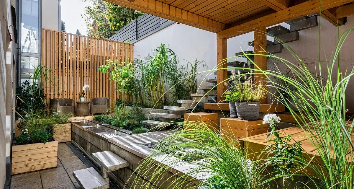 Giardini fioriti idee: un angolo zen con vasca d'acqua, gradini in pietra, sedute in legno e piante rigogliose sotto un pergolato.