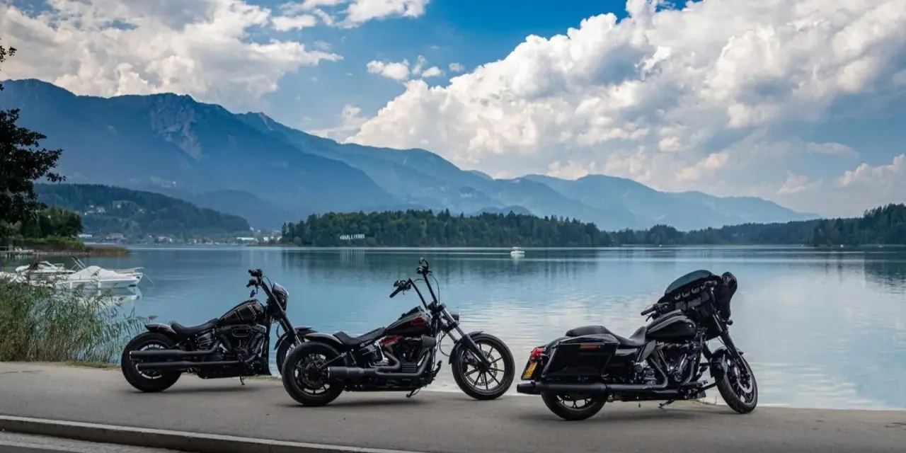 Tre moto parcheggiate sul lungolago, pronte per il faaker see motoraduno. Montagne sullo sfondo, cielo azzurro con nuvole bianche.
