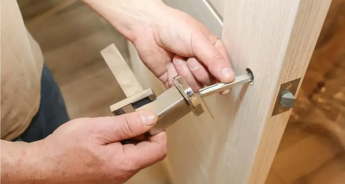 Hands assembling a modern door handle. A metal spindle is being inserted into the door mechanism, showing how to replace door handle.