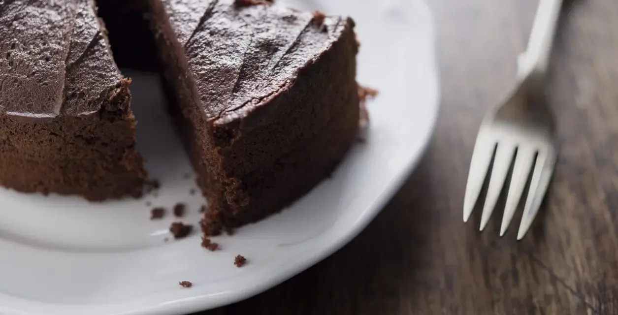 Una fetta di torta al cioccolato su un piatto bianco, con una forchetta accanto. Un'opzione deliziosa per chi cerca dolci senza zucchero.
