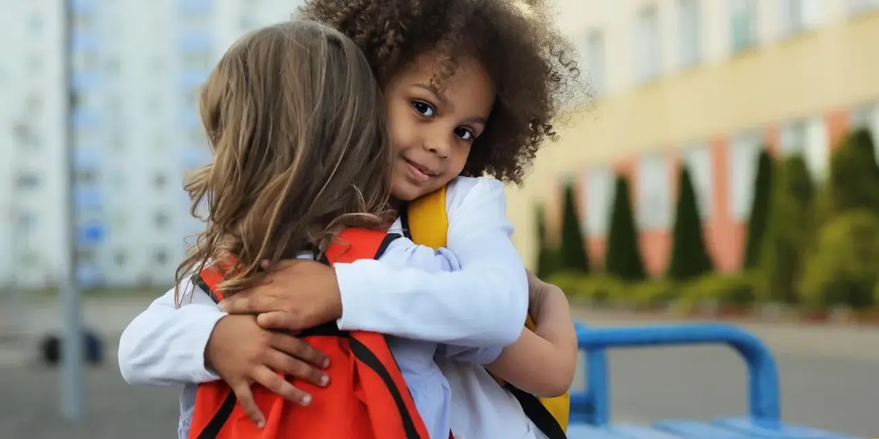 Zwei Kinder umarmen sich. Ein Mädchen mit Locken lächelt in die Kamera. Ein schönes Beispiel für Empathie bei Kindern.