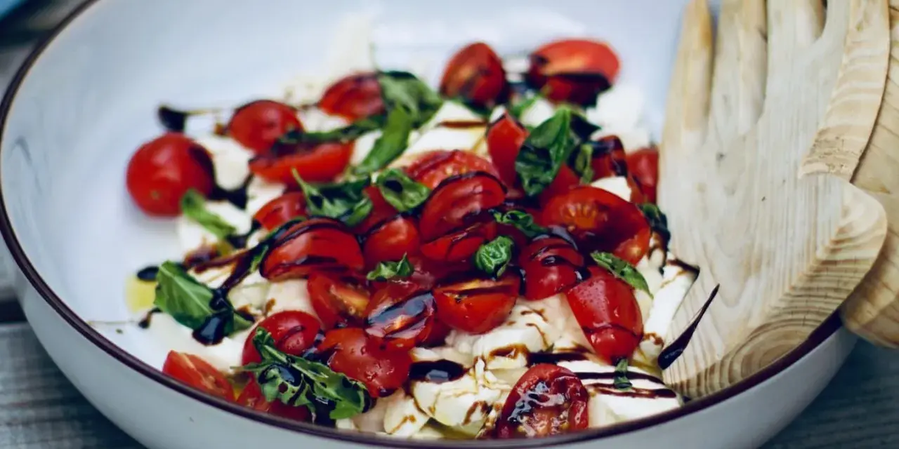 Frische Insalata Caprese mit saftigen Tomaten, cremigem Mozzarella und Basilikum, beträufelt mit Balsamico.