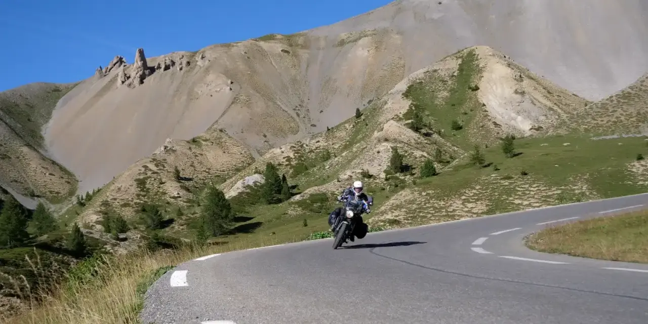 Motociclista percorre la route de grand alpes tra montagne scoscese e cielo azzurro.
