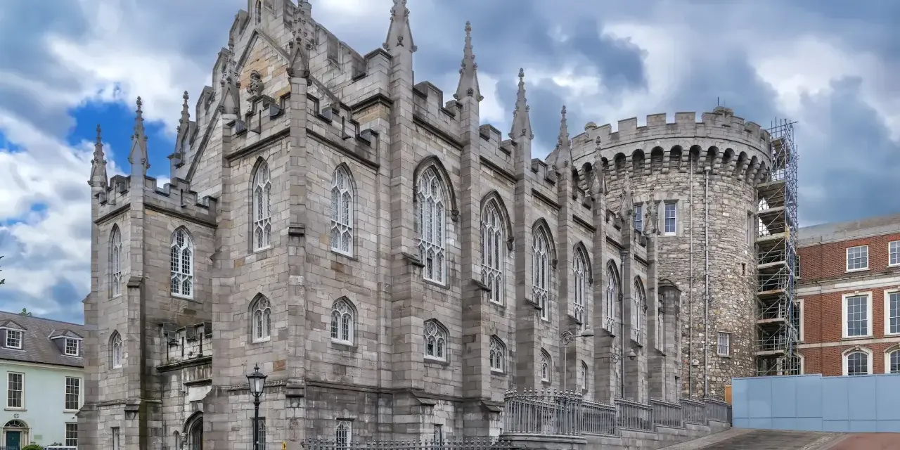 Kamienne mury i strzeliste wieże zdobią zamek w Dublinie. Gotycka architektura i chmurne niebo tworzą majestatyczny widok.