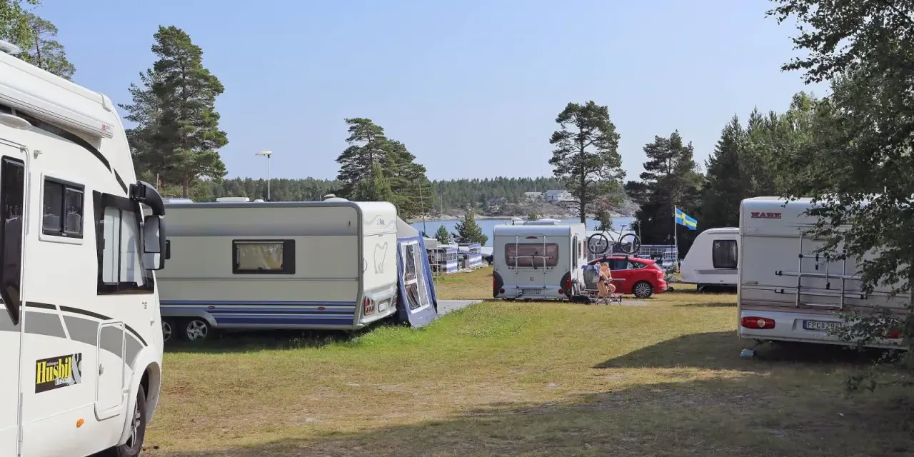 Solig dag på camping norrlandskusten med husbilar och husvagnar uppställda nära vattnet.