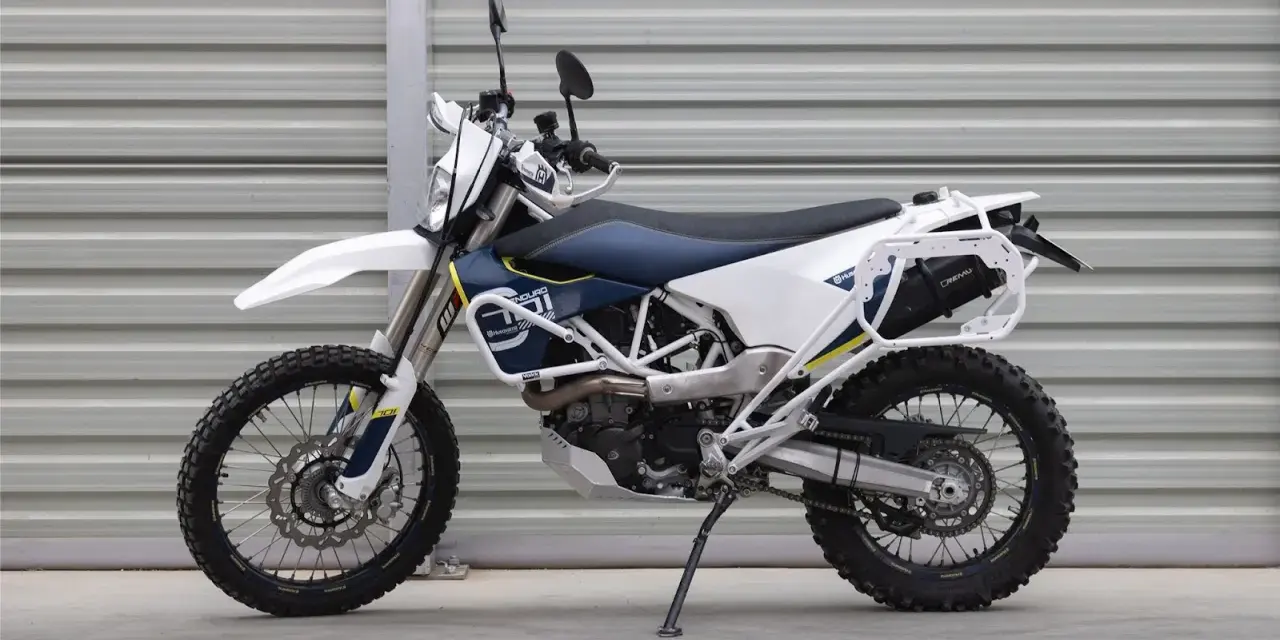 Biało-niebieski motocykl Husqvarna z bagażnikiem, gotowy na przygody w terenie. To idealny sprzęt do lekkiego enduro.