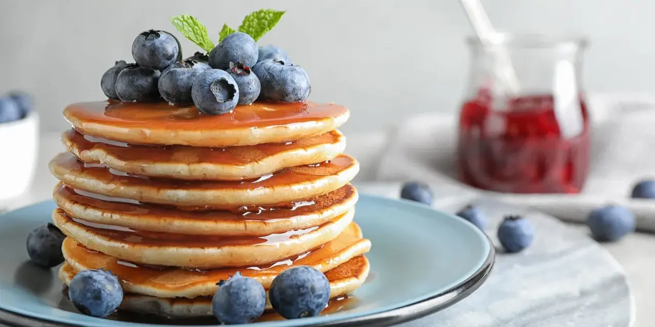 Stos puszystych pancakes polanych syropem, ozdobiony jagodami i miętą. Idealny przepis na pancake na śniadanie.