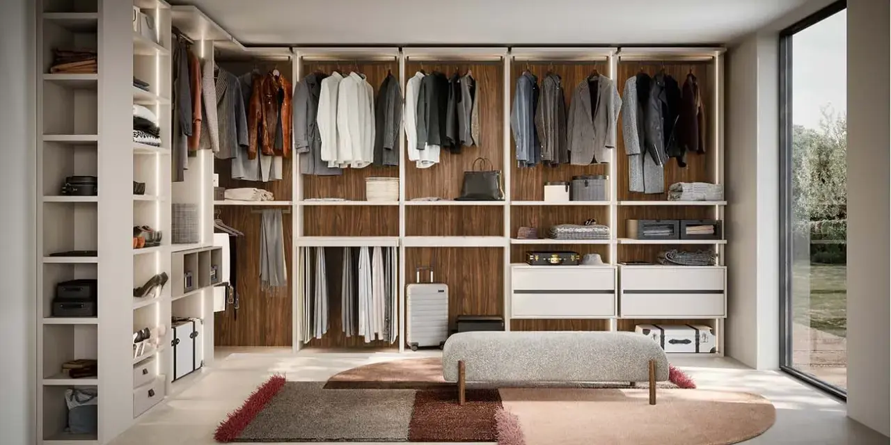 Ampia cabina armadio stanza con scaffali a vista, abiti appesi, cassettiere e un pouf centrale.