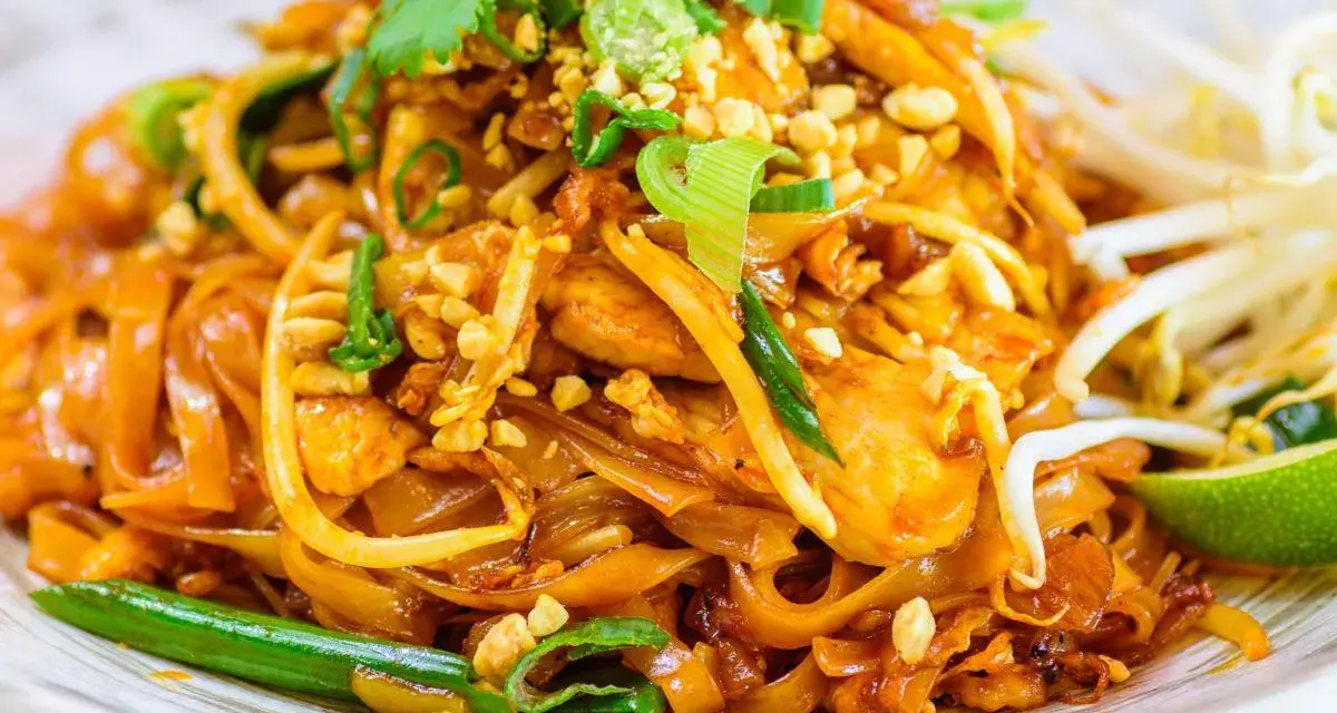 Un delicioso plato de pad thai con fideos de arroz, pollo, brotes de soja, cacahuetes picados y cilantro fresco.