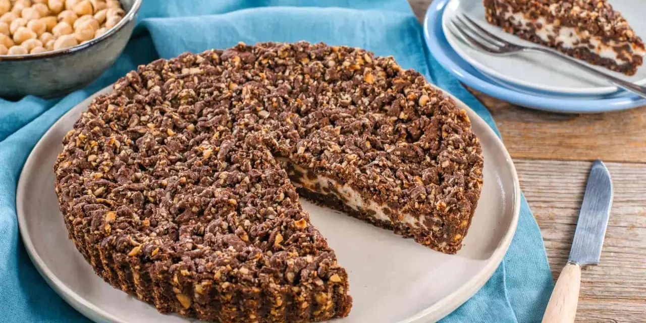 Sbriciolata ricotta e cioccolato con croccante copertura di nocciole. Una fetta invitante attende su un piattino.