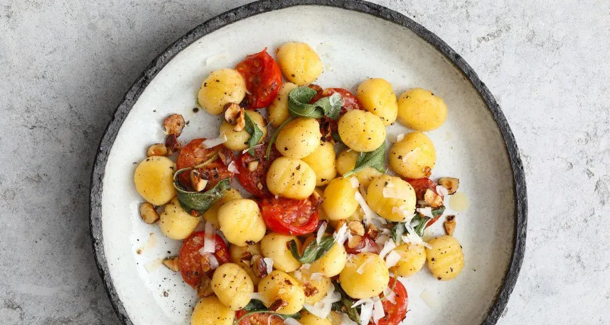 Pyszne makaron gnocchi z pomidorkami, szałwią i orzechami na talerzu.