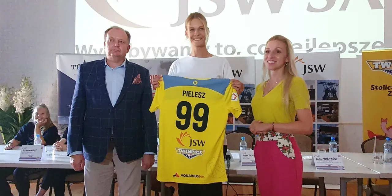 Trzy osoby pozują z koszulką z numerem 99 i nazwiskiem PIELESZ. W tle logo JSW i napisy związane z firmą, być może z okazji wydarzenia w MTS Żory.