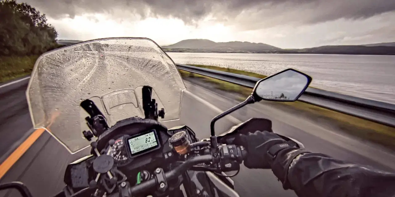 Jazda motocyklem w deszczu w kierunku Nordkapp. Pochmurne niebo i mokra droga nie zniechęcają do podróży.