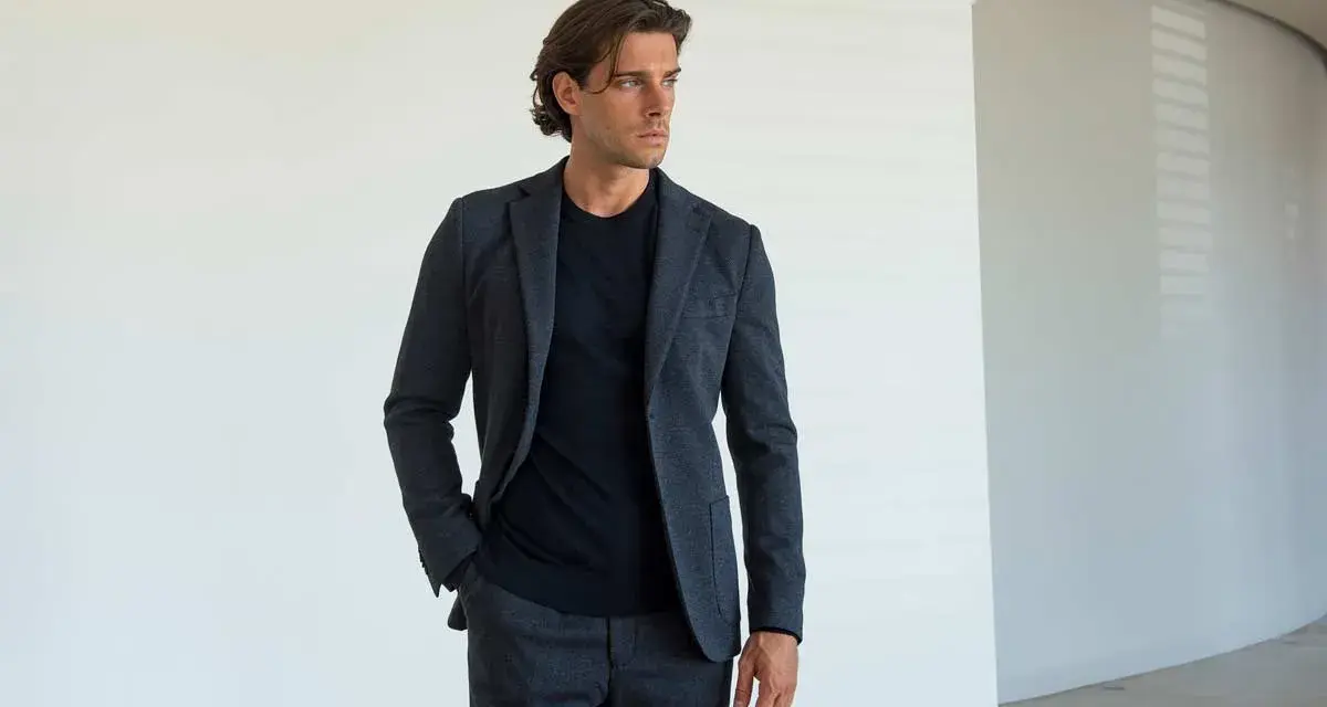 Uomo con giacca e pantaloni grigi, una mano nella tasca laterale del pantalone, mostrando i diversi tipi di tasche pantaloni uomo.