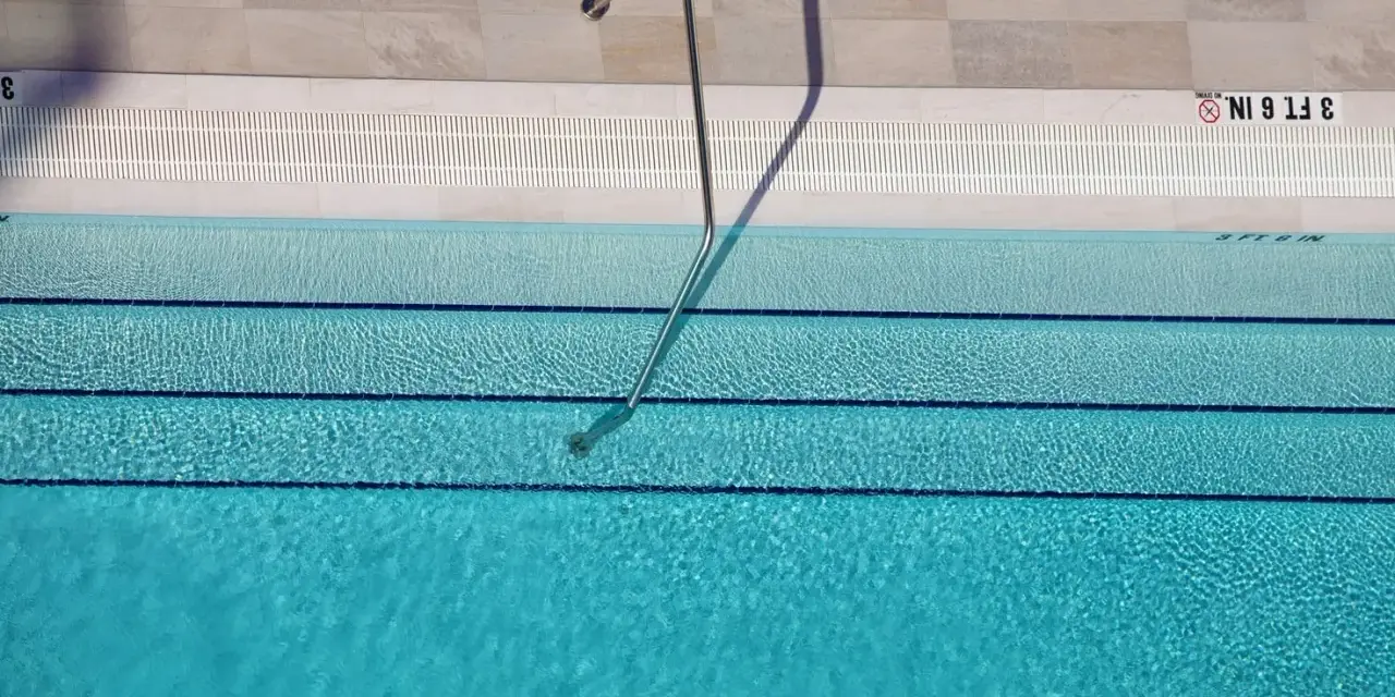 Escalera metálica en piscina de agua clara, con marcas de profundidad. El mantenimiento de piscinas es clave para su disfrute.