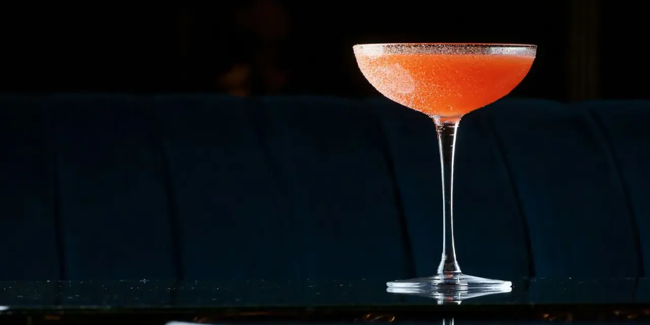 Orzeźwiający el presidente cocktail, z pomarańczowym odcieniem i cukrową obrączką, stoi na błyszczącym blacie.