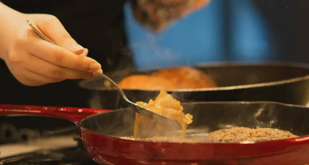 Cebolla caramelizada siendo removida con un tenedor en una sartén roja sobre el fuego.