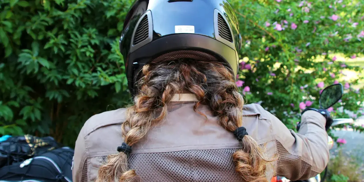 Donna con casco nero e capelli raccolti in due trecce, pronta per legare il casco alla moto.