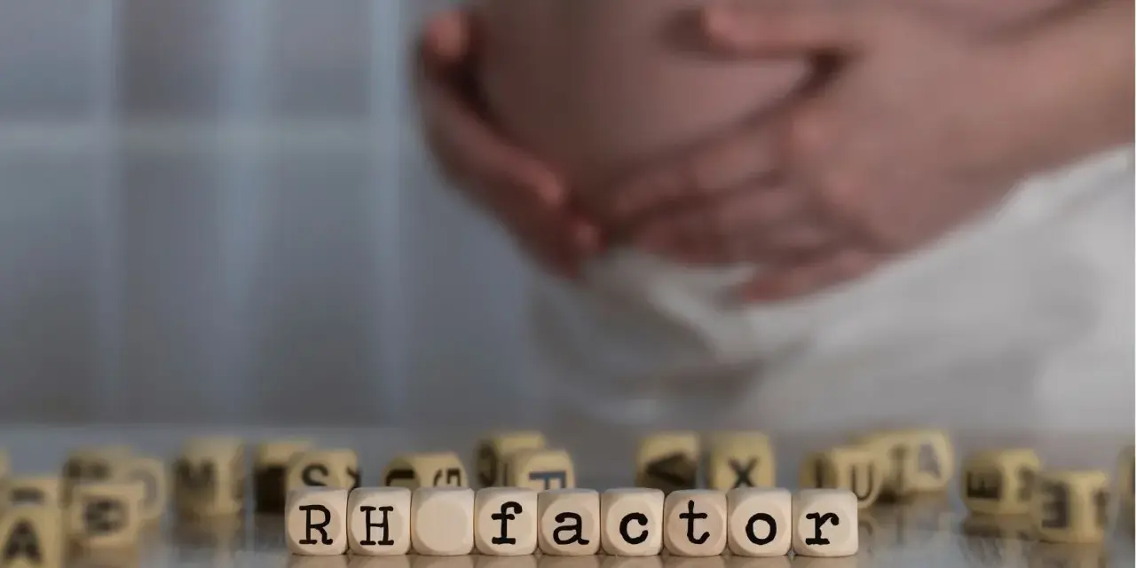 Ciąża i czynnik Rh. W tle brzuch kobiety, na pierwszym planie kostki z napisem "RH factor". Immunoglobulina w ciąży może być kluczowa.
